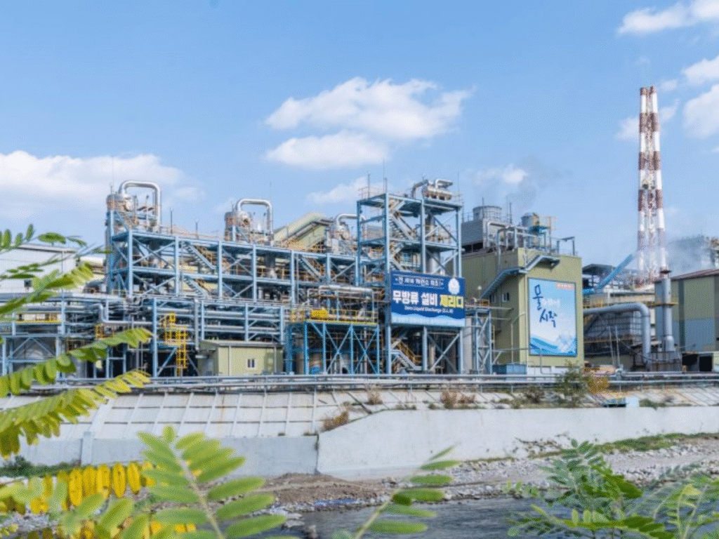 Industrial zinc processing plant in South Korea with complex steel structures, pipes, and chimneys under a partly cloudy sky.