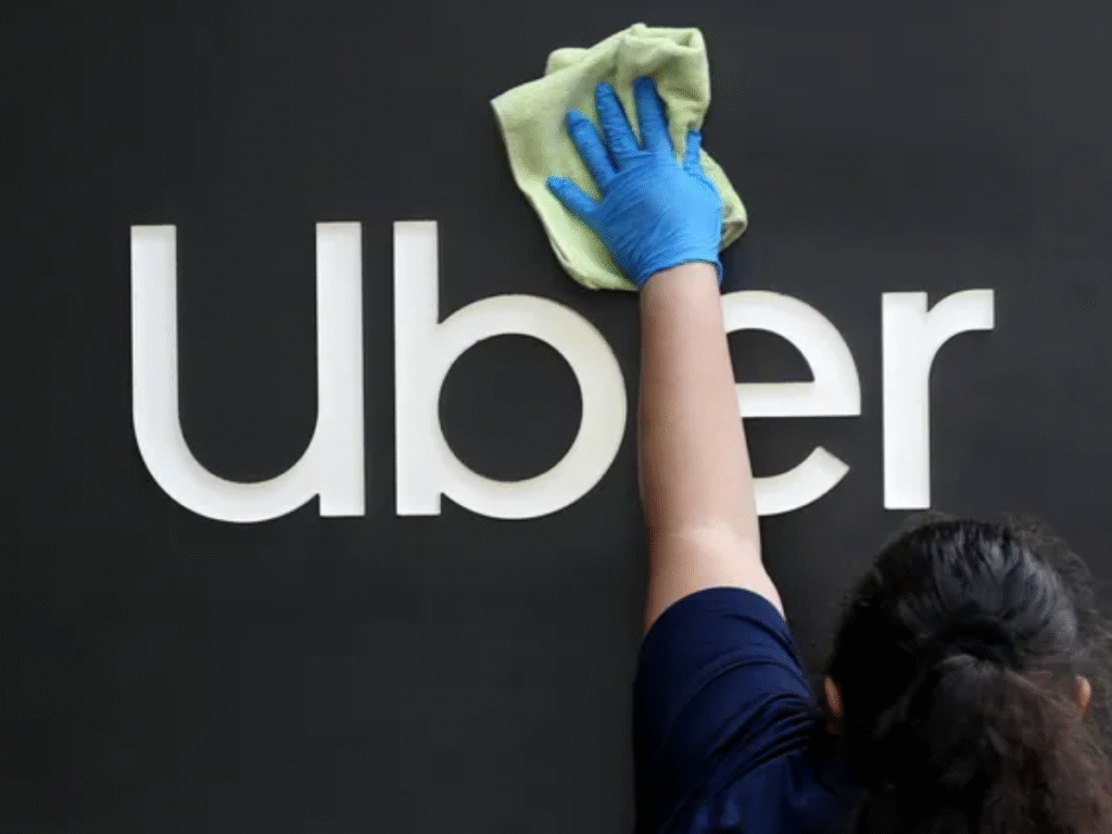 A worker wearing blue gloves wipes the Uber logo on a black background using a cloth.