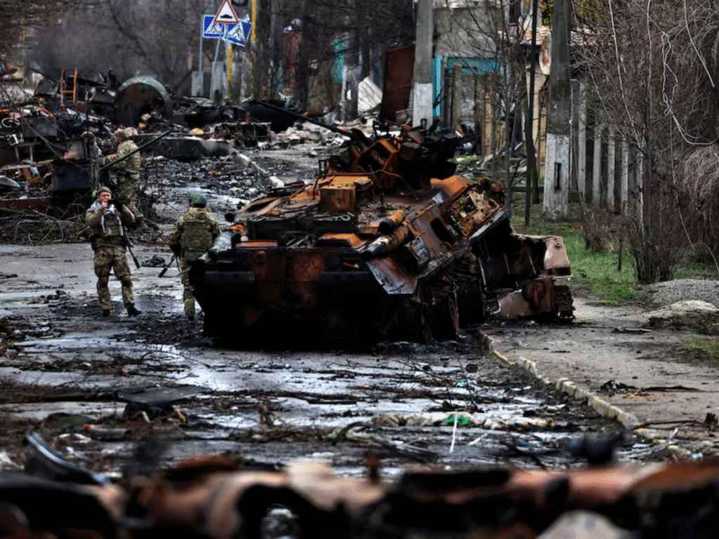 Ukrainian soldiers walk through a damaged street filled with destroyed military vehicles and debris during ongoing fighting.