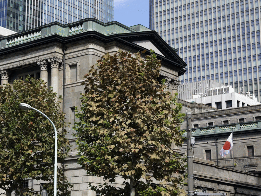 Exterior view of the Bank of Japan headquarters in Tokyo with surrounding trees and nearby office buildings.
